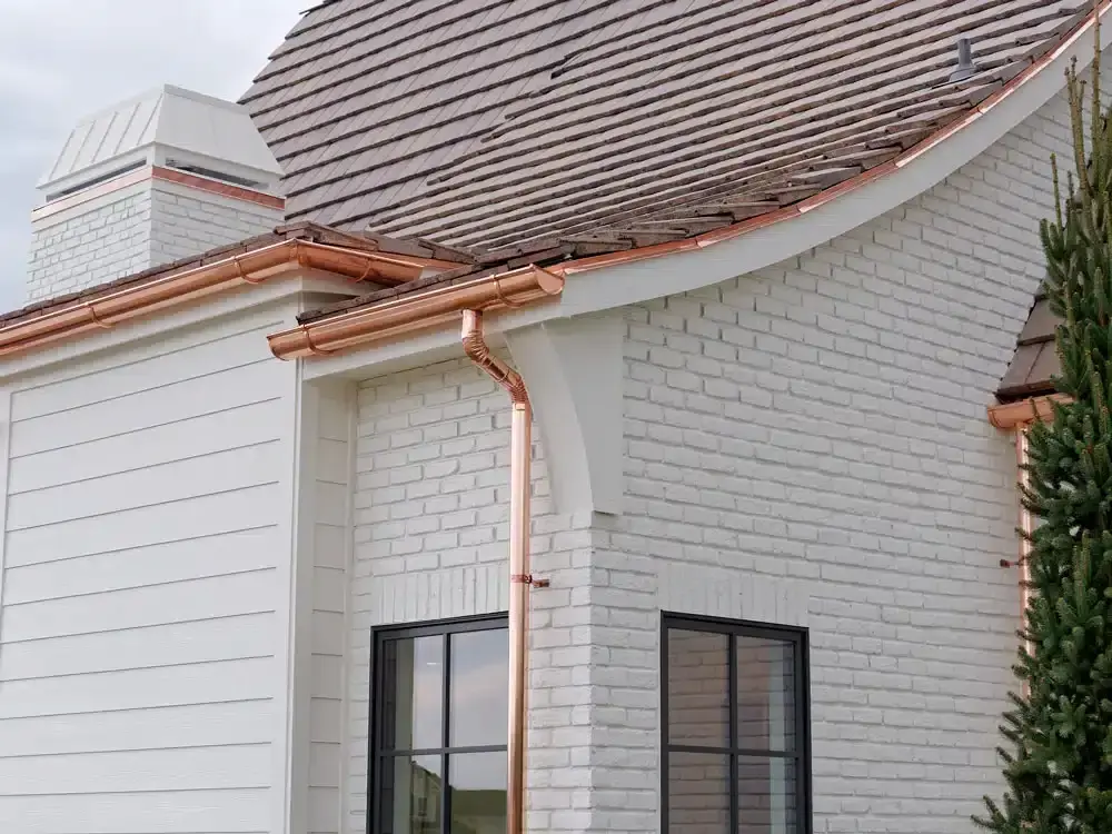 Copper gutters on the side of a white brick house, illustrating high-end gutter replacement options.